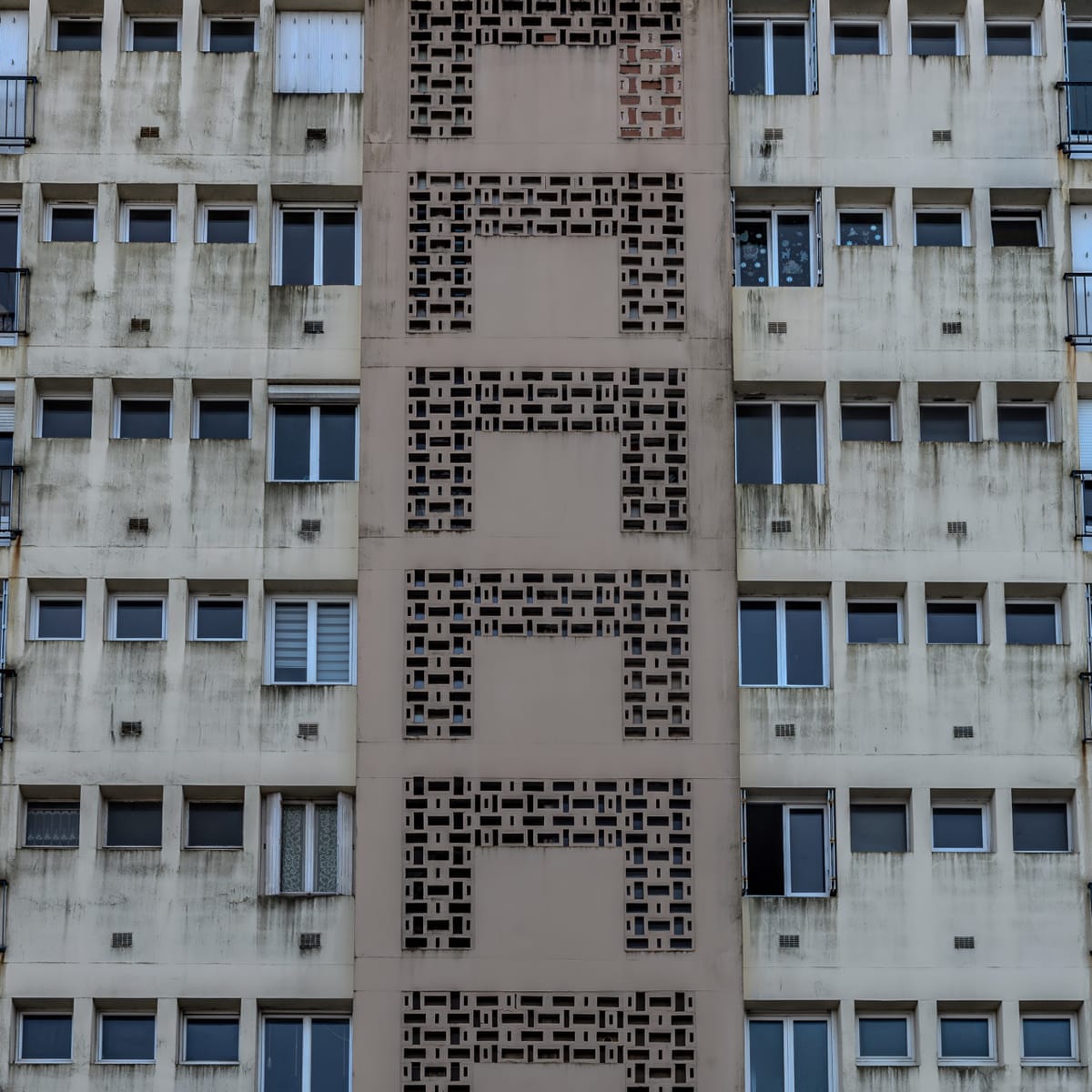 Façade d'immeuble à Quimper, avec une colonne centrale de claustras géométriques perforant le béton gris